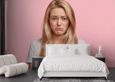 Portrait of displeased upset female frowns face as going to cry, being discontent and unhappy as can`t achieve goals, isolated over pink studio background. Dissapointed young woman has troubles Wall mural